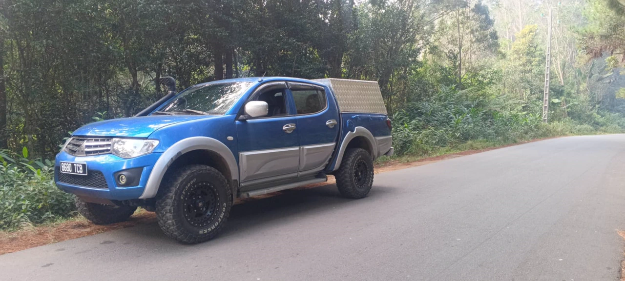 Mitsubishi L200 pickup driving through forest on a red clay track in Madagascar