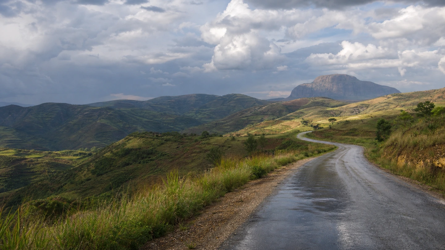 Green mountain landscape with a rain-wet road beneath changing skies in Madagascar