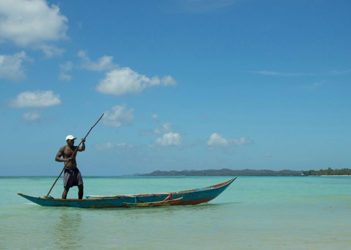 A fisherman paddles a traditional canoe in the clear waters of Madagascar under a blue sky.